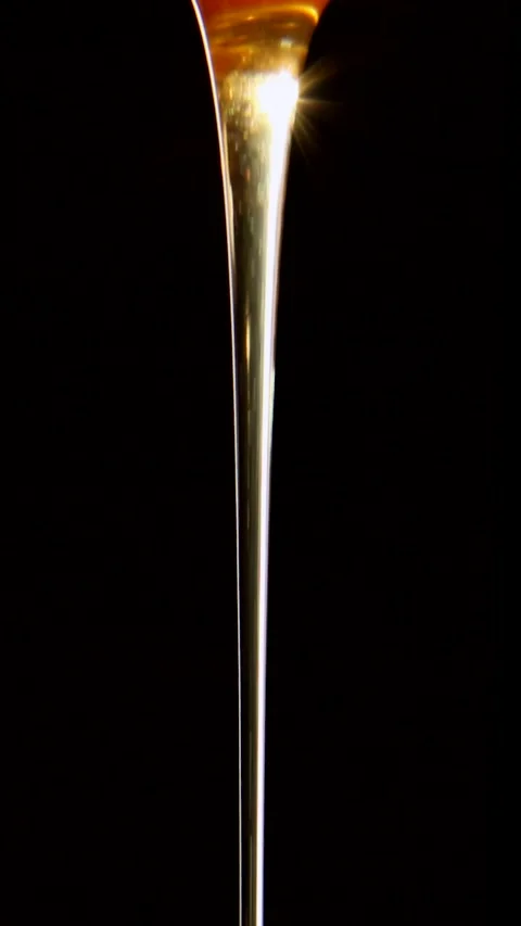 A continuous stream of honey illuminated by the sun on a black background. Stock Footage 246620245