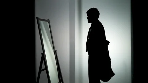 The contour of an unrecognizable young man in front of the window, put on blazer Stock Footage 118938595