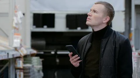 Contractor browsing building materials on a smartphone in a lumber yard or home Stock Photos