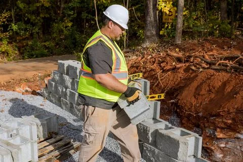 A contractor is constructing a block retaining wall on a construction site while 스톡 사진