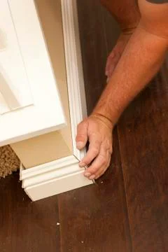 Contractor Fitting New Baseboard to Wall and New Laminate Flooring Abstract. Stock Photos