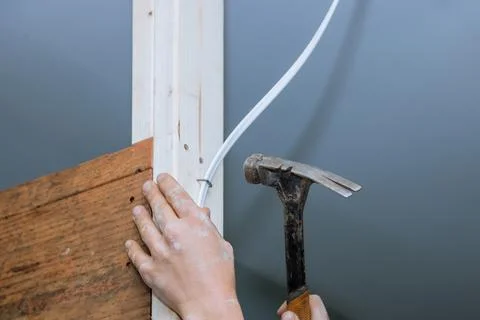 Contractor hand grips hammer while another adjusts electrical wiring against Stock Photos