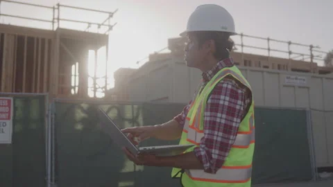 Contractor in Hard Hat and Safety Vest Types on Computer at Job Site in sunshine Stock Footage 208783216