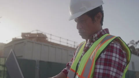Contractor in Hardhat Looks at Blueprints on Computer at Construction Site Stock Footage 208782602