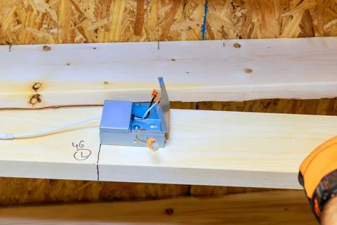 Contractor is installing an electrical box on wooden beam in building under c Stock Photos