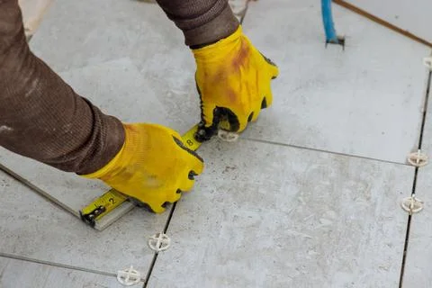 As a contractor prepares to lay ceramic tiles on a floor, he measures the tiles Stock Photos