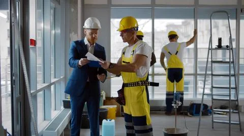 Contractor talking with builder in uniform and hardhat discussing office 写真素材