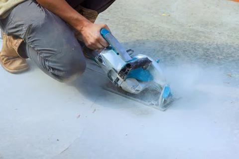 Contractor is using concrete cutter saw on ground at construction location du Stock Photos