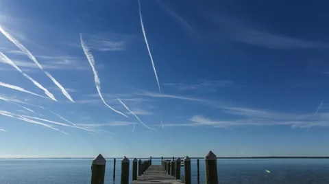 Contrails in the sky passing over a dock timelapse Stock Footage