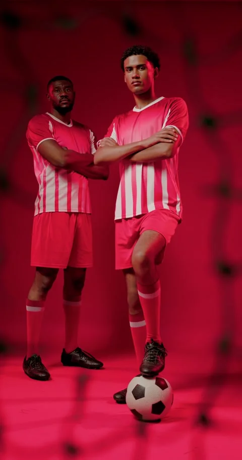 Controlling lead player placing foot on soccer ball in red studio, blurred net Stock Footage 345040901