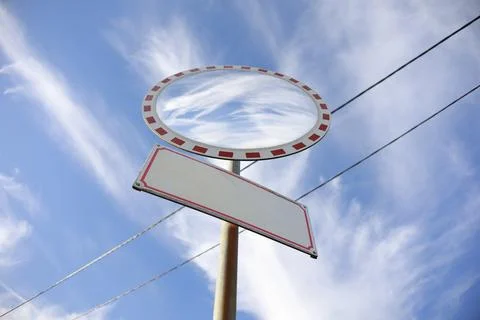 Convex traffic mirror and empty signboard on the pole and post. Blue sky with Stock Photos