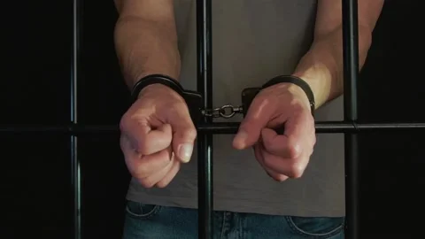 A convicted man is handcuffed in a cell behind bars on a dark background. Concep Stock Footage 194535344