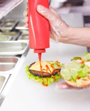 Cook adding a ketchup on burger. Fotos Stock