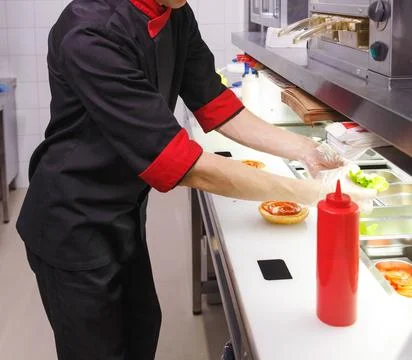 Cook adding a ketchup on burger. Фото