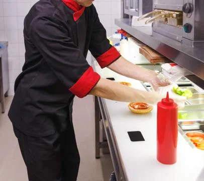 Cook adding lettuce on burger. Fotos Stock