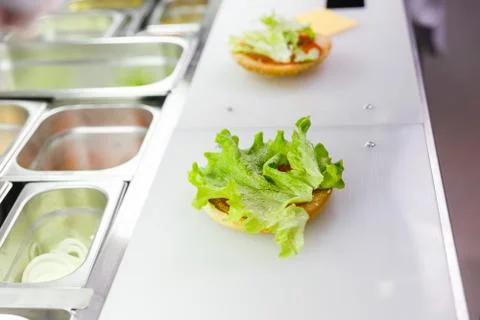 Cook adding lettuce on burger. Preparing burger in restaurant. Stock Photos