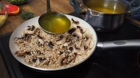 Cook adding more vegetable bullion to barley mushroom risotto in a pan Stock Footage 88110971
