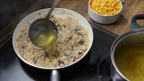 Cook adding more vegetable bullion to barley mushroom risotto in a pan Video stock 88110986