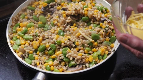 Cook adding shredded vegan cheese to barley risotto with fava bean and mushrooms Stock Footage 88111003