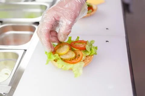 Cook adding slices of pickled cucumber on burger. Stock Photos