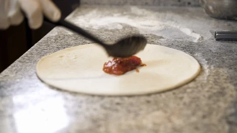 Cook adding tomato paste with a cooking spoon to pizza dough base Stock-Footage 105347749