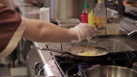 The cook adds a raw egg to a hot frying pan on a gas stove Stock Footage 76146907