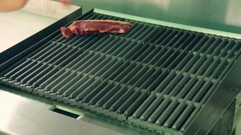 The cook adds raw meat steaks on a hot grill Stock Footage 127715482
