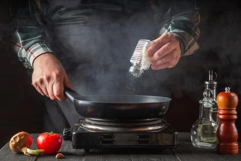 The cook adds salt while cooking food in the pan. Working environment Stock Photos