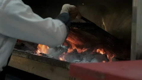 The cook adjusts the fire and embers of the grill. Fire and grill footage 4k. Stock Footage 233067215