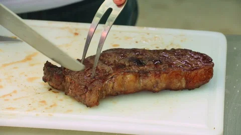 Cook with a big fork and a knife slicing perfectly cooked juicy steaks. Stock Footage 127715623