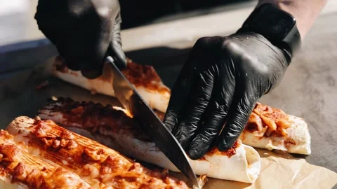 A cook in black gloves cuts a cooked shawarma for a treat. Close-up shooting Stock Footage 336659496