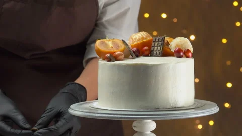 Cook in black gloves is decorating cake with cranberries, persimmons, tangerines Stock Footage 167009542