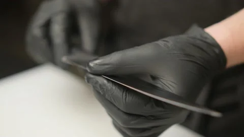 The cook in black gloves, draws with two fingers along the blade of a knife. Stock Footage 236251729