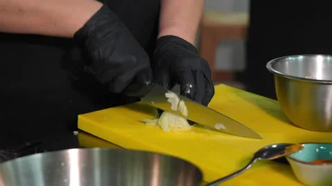 Cook in black gloves is slicing white onions on yellow board in kitchen. 스톡 동영상 267291220