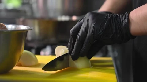 Cook in black gloves is slicing white onions on yellow board in kitchen. 스톡 동영상 267667849