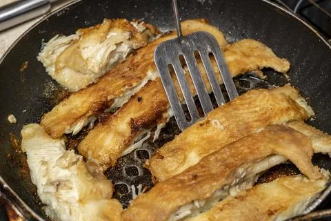 The cook checks the readiness of the fish with a fork Foto stock