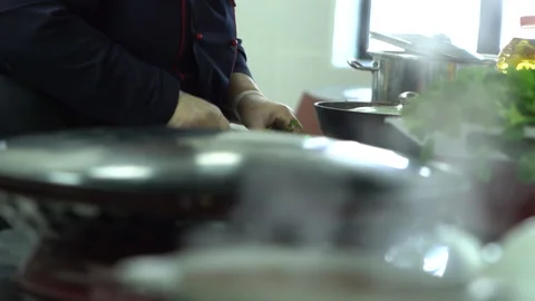 The cook is chopping herbs next to the boiling cauldrons in the kitchen Stock Footage 234829735