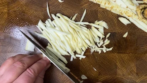 A cook chops parsley root with a knife on a wooden cutting board. Vídeo Stock 302753482