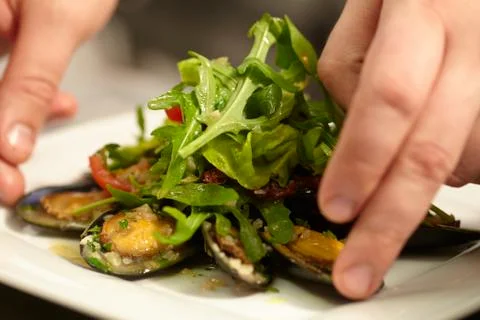 Cook collects a dish of clams and greens arugula salad with mussels Stock Photos