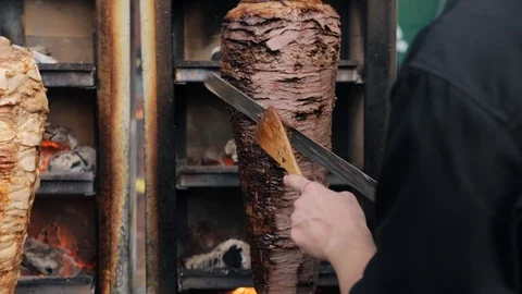 A cook cuts beef to make shawarma, gyros, doner kebab. Cooking meat on a skewer Stock Footage 105779162