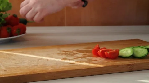Cook cuts cherry tomato and cucumber with kitchen knife on wooden cutting board Stock Footage 144792859