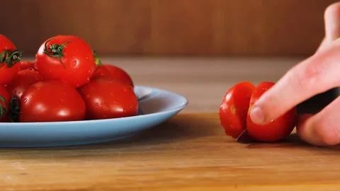 Cook cuts cherry tomato with large kitchen knife on wooden kitchen cutting board Stock Footage 144792812