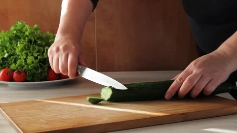 Cook cuts cucumber with large kitchen knife on wooden kitchen cutting board. Stock Footage 144792846