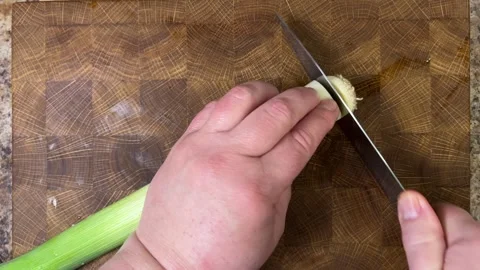 A cook cuts leek stems with a kitchen knife on a wooden cutting board.	 Stock Footage 302283754