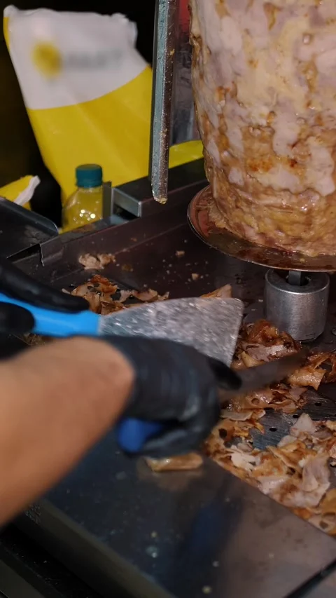 A cook cuts meat to make shawarma, gyros, doner kebab. Cooking Meat on a skewer Stock Footage 313864218