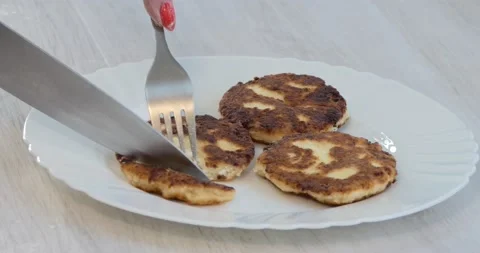 The cook cuts off a piece of cooked curd fritter lying on a plate with a knife . Video stock 146256590