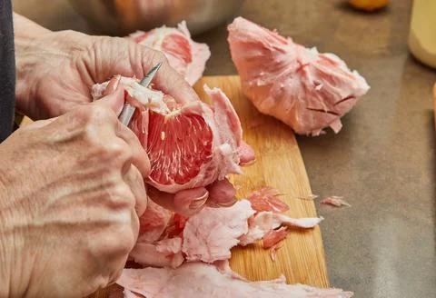 Cook cuts the pomelo red inside into slices and removes the skin on cutting Stock Photos