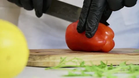 A cook cuts a red pepper in half with a knife on a chopping Board, slow motion. Stock Footage 135555510