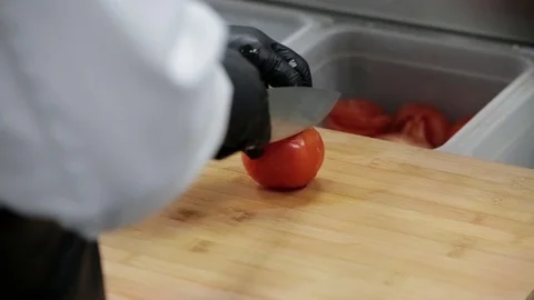 The cook cuts a red tomato with a sharp knife on a cutting board Stock Footage 127197180