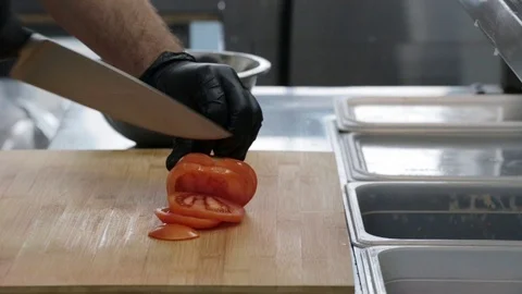 The cook cuts a red tomato with a sharp knife on a cutting board Stock Footage 127202218